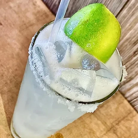 Milky white margarita with frothy top, salt rim, and lime wedge.