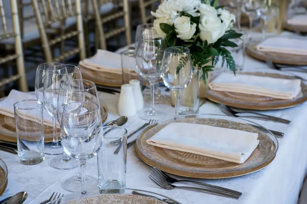 Formal dining table set with gold chargers, white roses, and place settings.