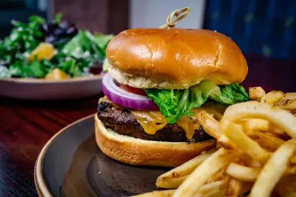 Cheeseburger with melted cheese, fries, and salad on a dark plate.