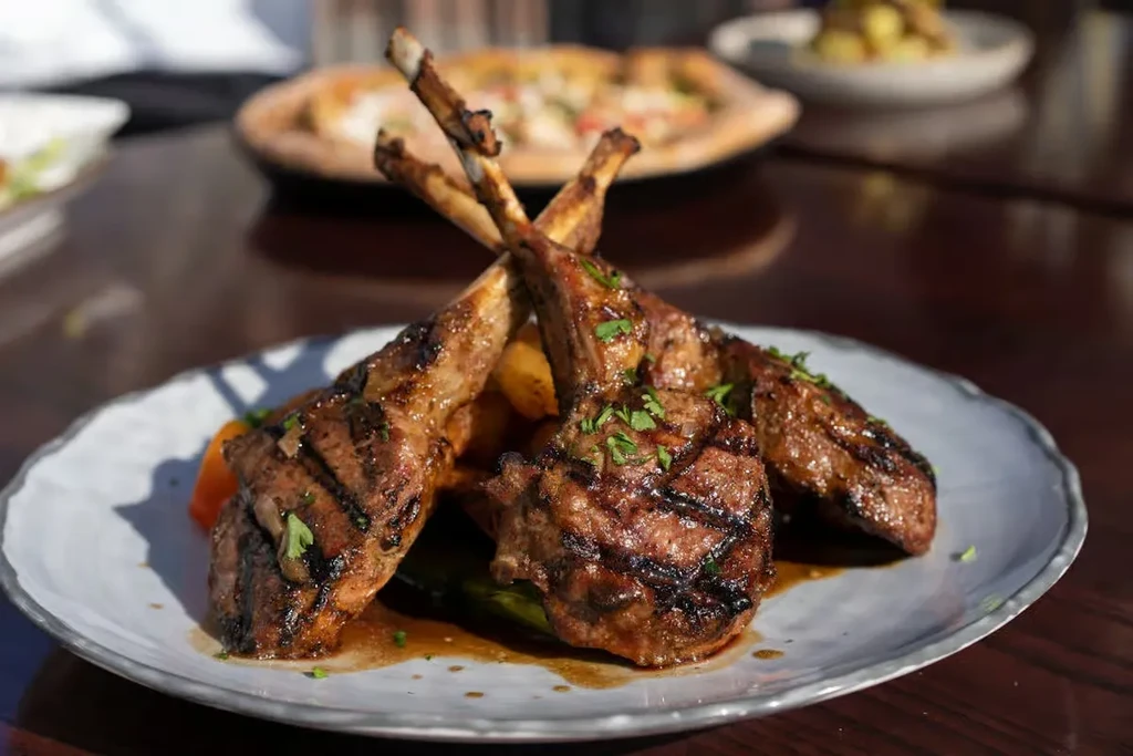 Grilled lamb chops with vegetables and sauce on a plate.