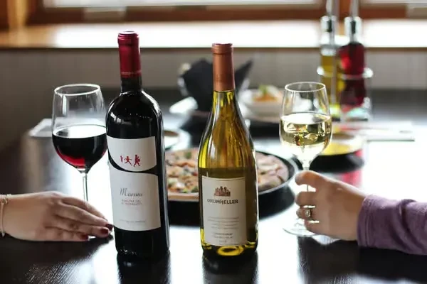 Two hands, red and white wine bottles and glasses on a table.