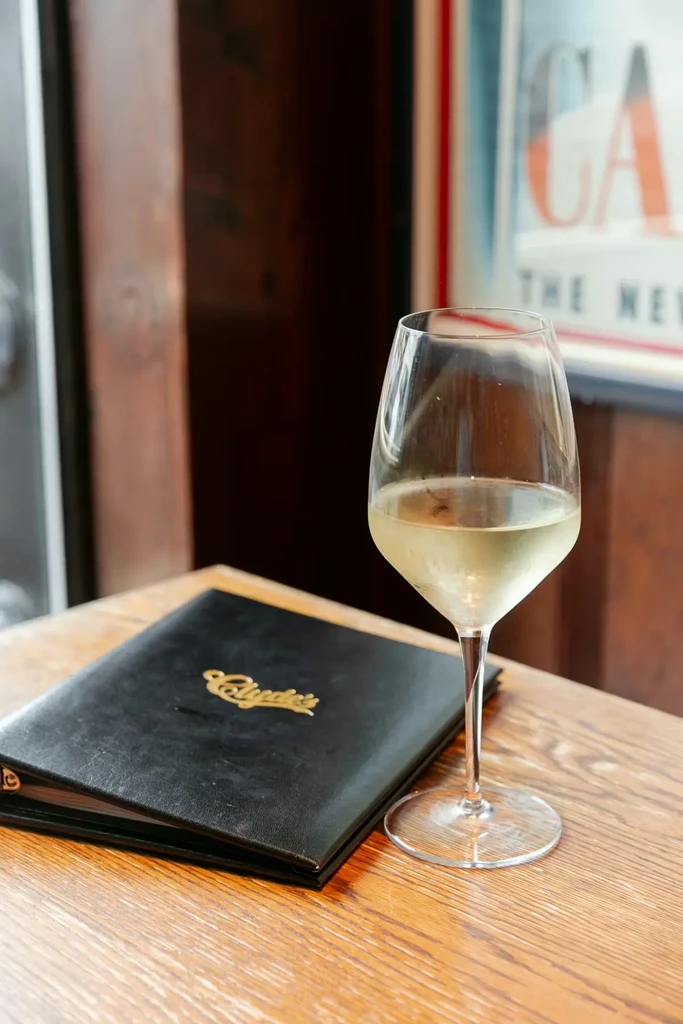 Half-filled white wine glass and 'Clyde's' menu on a wooden table.