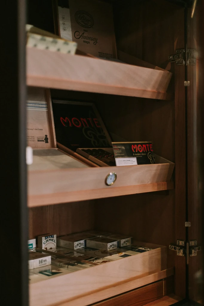 Wooden humidor cabinet filled with Montecristo cigars and Camel cigarettes.