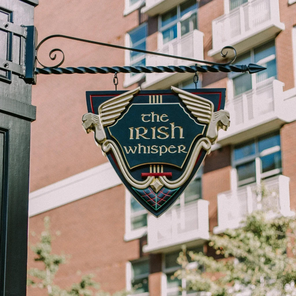 Ornate hanging sign for 'The Irish Whisper' with gold and winged creatures.