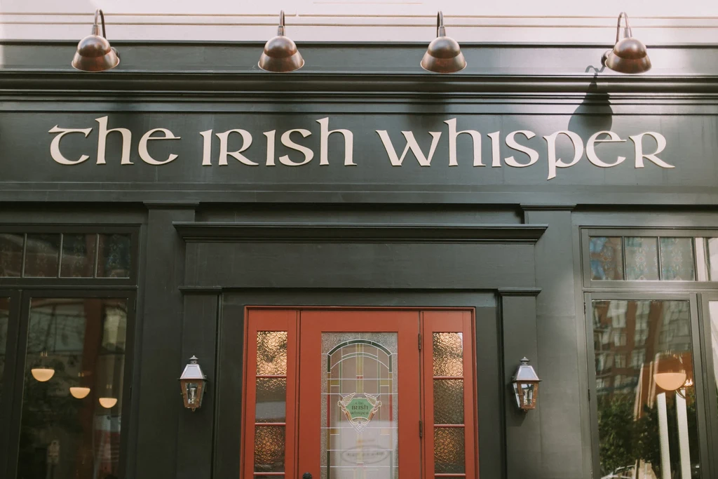 The Irish Whisper pub entrance: dark green facade, red doors, classic signage.