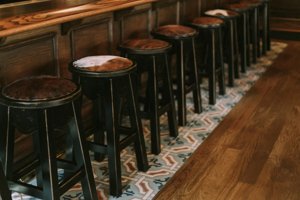 Empty bar stools with patterned hide seats line a dark bar.
