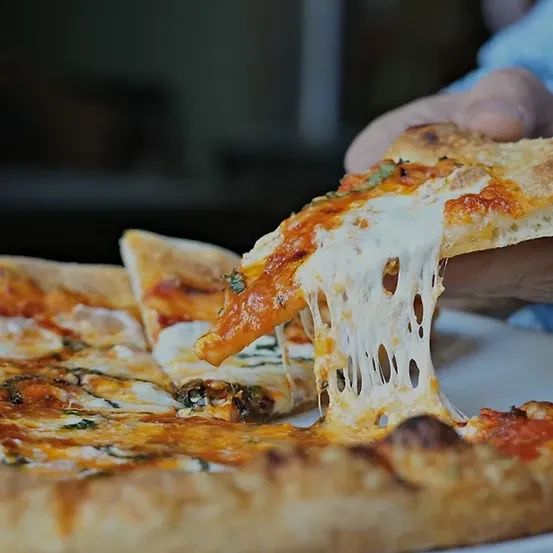 Close-up of a hand pulling a pizza slice with stretching cheese.