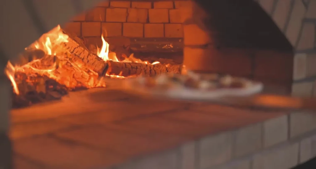 Blurred pizza on peel by bright wood fire in brick oven.