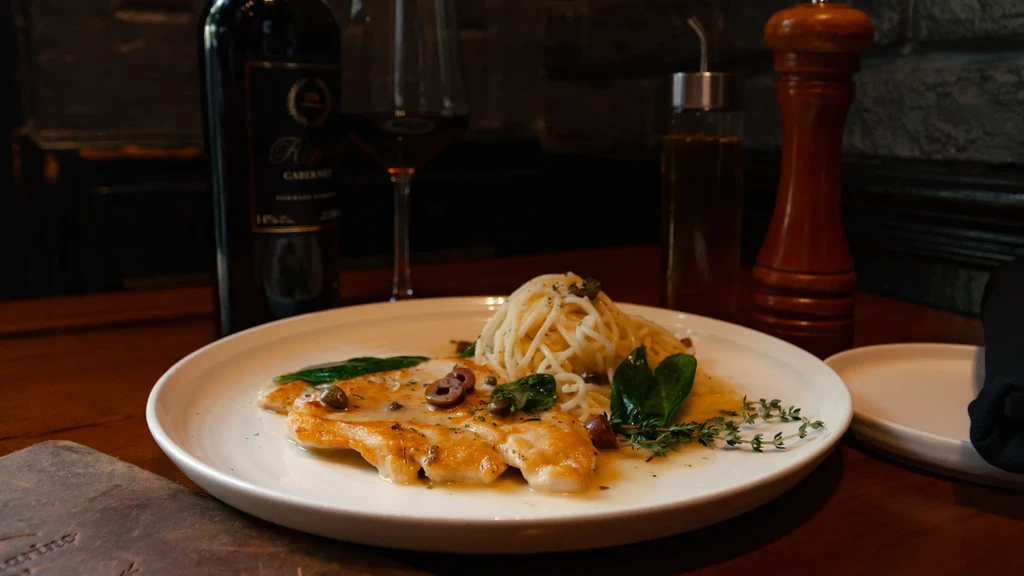 Plated golden-brown chicken or fish with spaghetti, wine, and pepper mill.