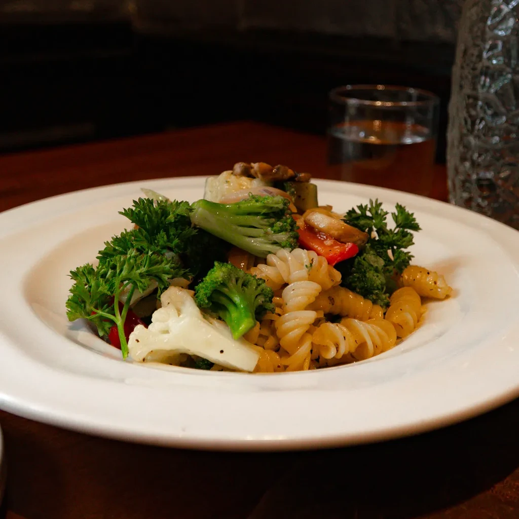 Fusilli pasta with broccoli, cauliflower, red pepper, and parsley on a white plate.