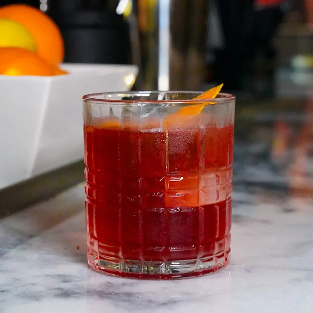 Red cocktail with ice, orange peel, in old-fashioned glass on marble.