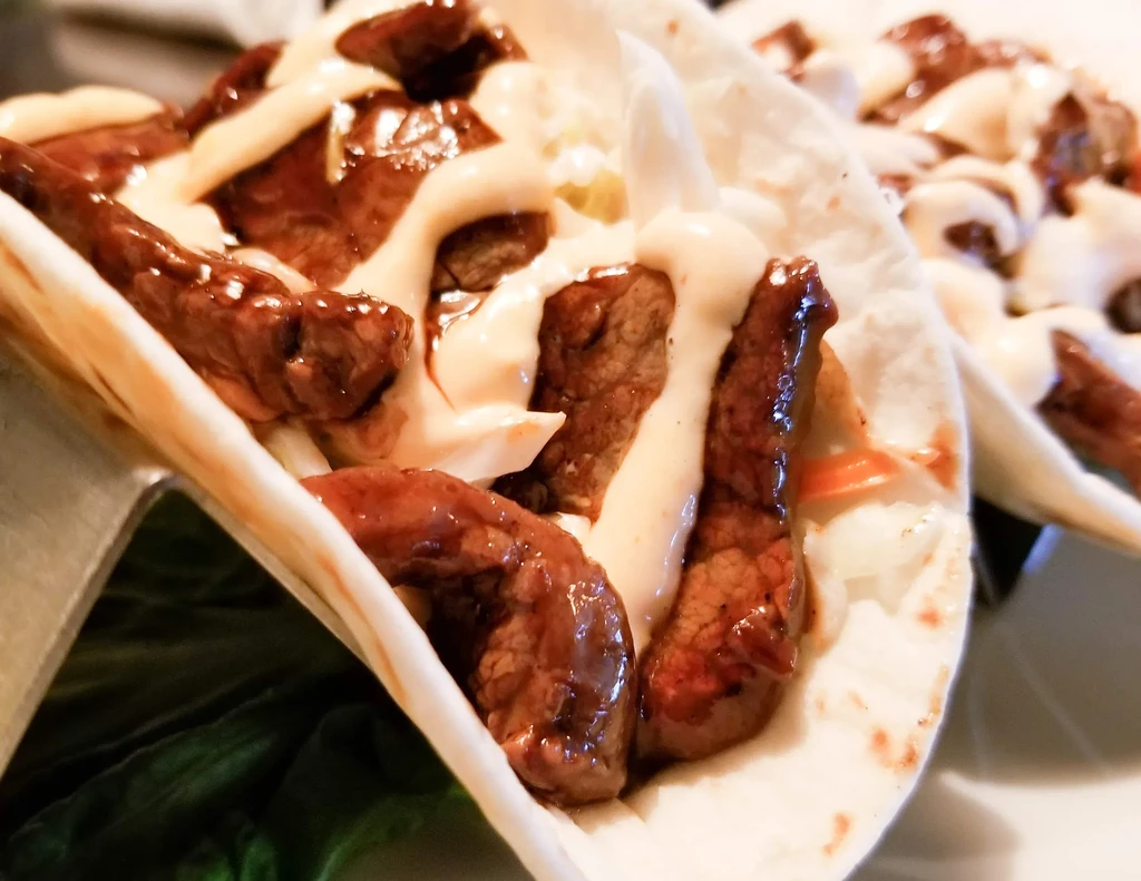 Two tacos with cooked meat, shredded white vegetables, and creamy sauce.