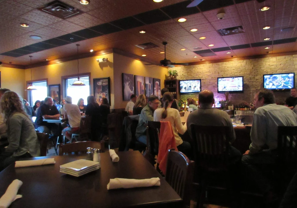 Busy casual restaurant interior with patrons, warm lighting, and TVs.