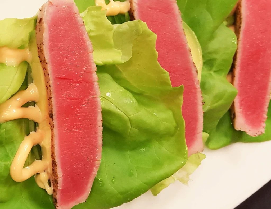 Seared rare tuna slices on lettuce wraps with orange sauce.