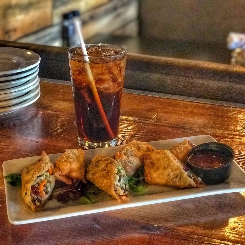 Fried spring rolls with dipping sauce and a drink on a wooden table.