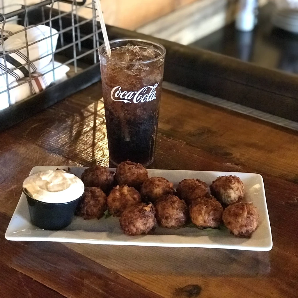 Fried appetizers, dipping sauce, and Coca-Cola on a wooden table.