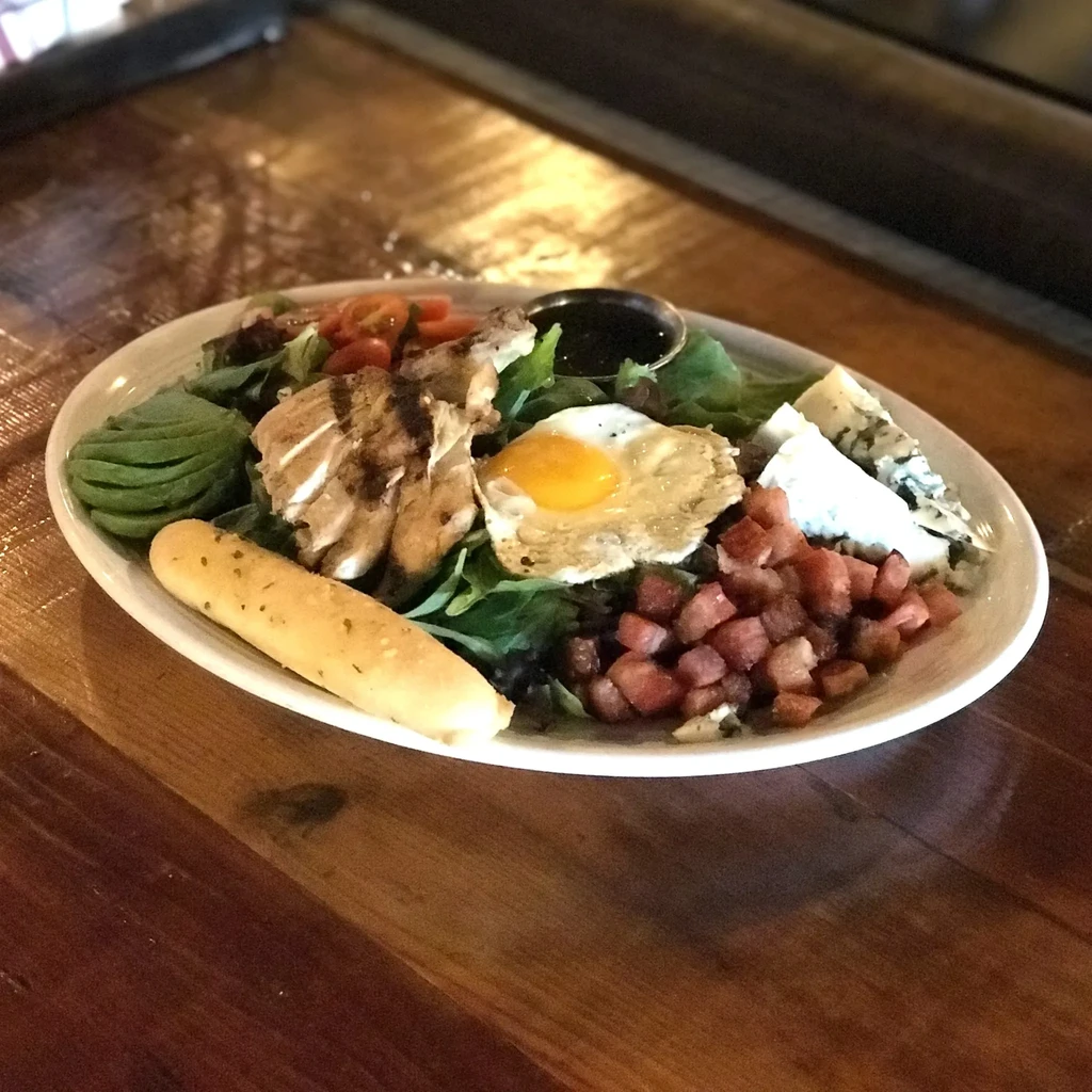 Plated chicken salad with fried egg, avocado, cheese, and dressing.