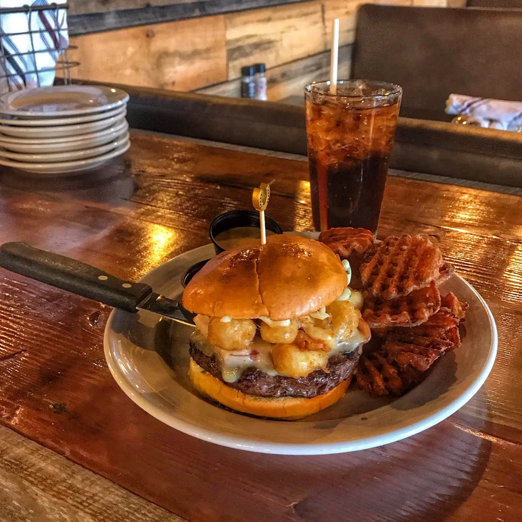 Burger with tater tots, melted cheese, waffle fries, and soda.