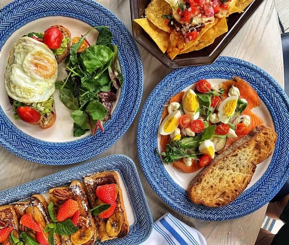 Overhead table with avocado toast, nachos, salmon salad, and French toast.
