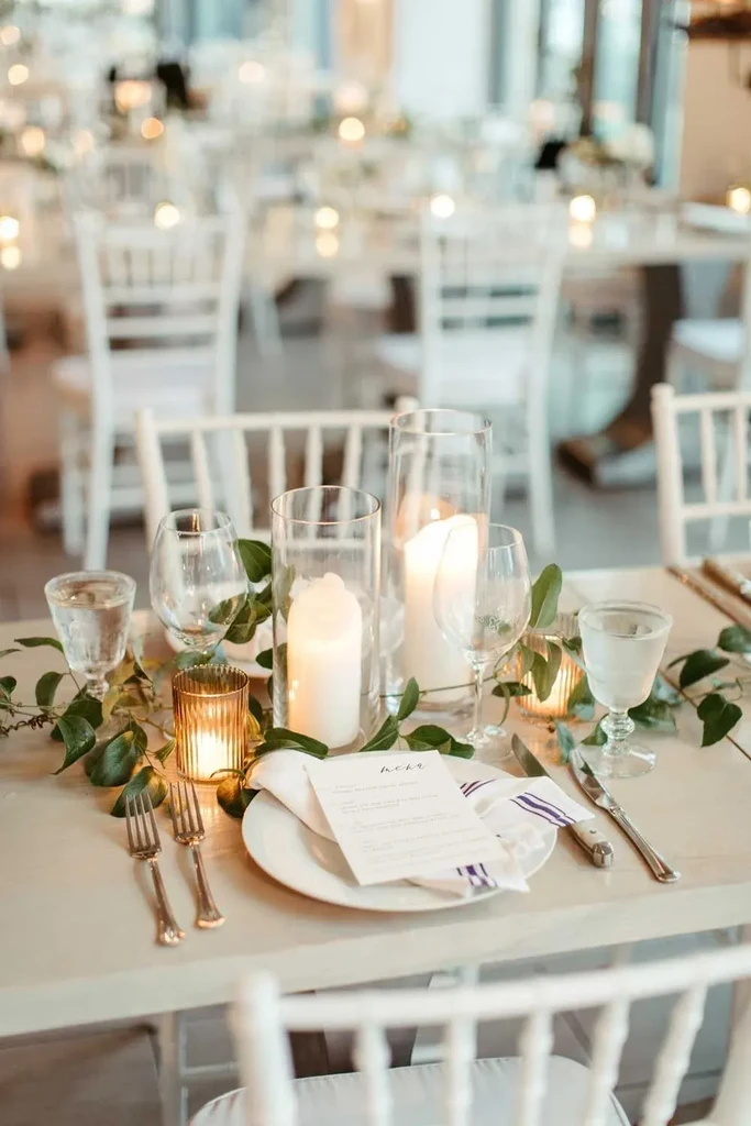 Elegant dining table with lit candles, green garland, and a place setting.