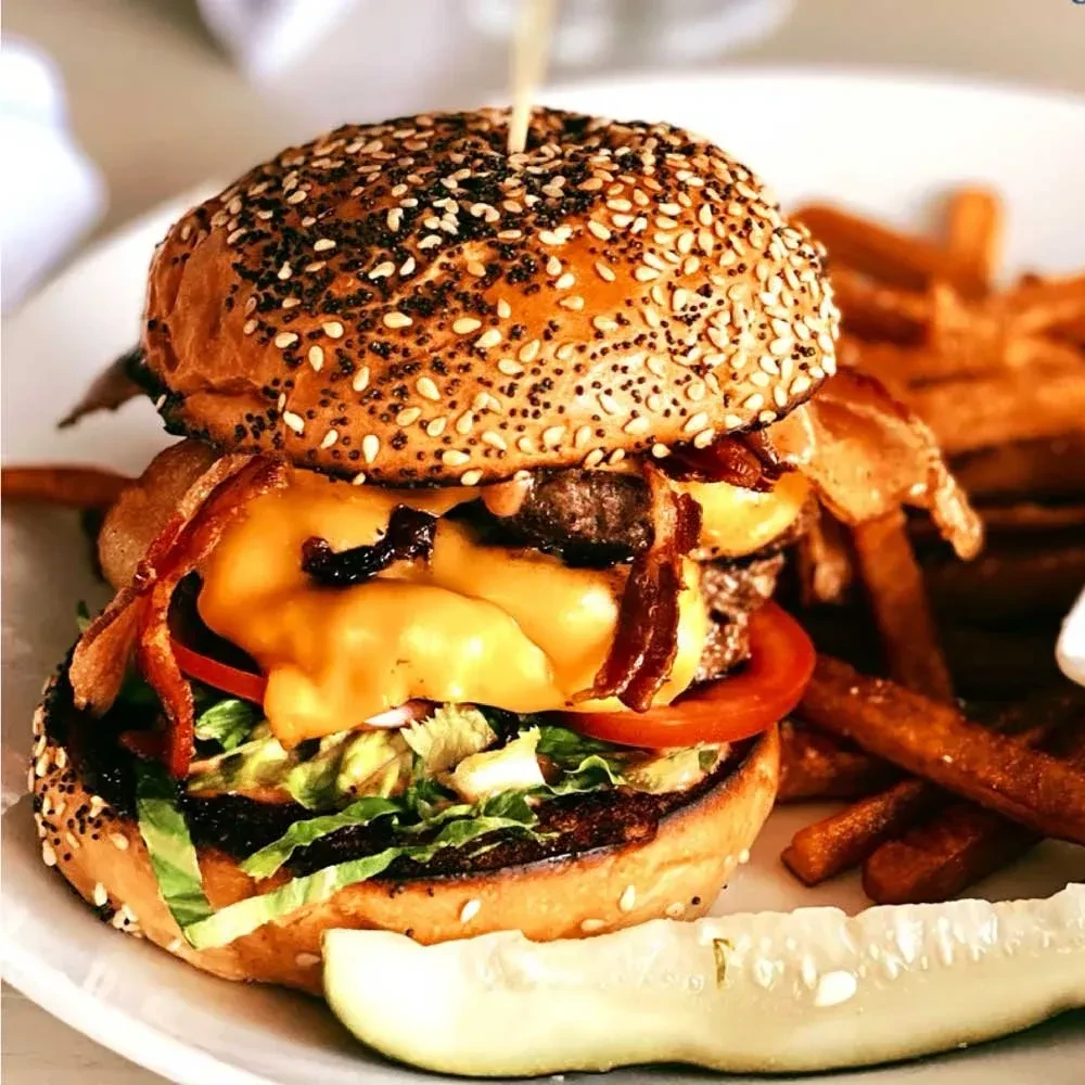 Tall burger with cheese, bacon, lettuce, tomato, fries, and pickle.