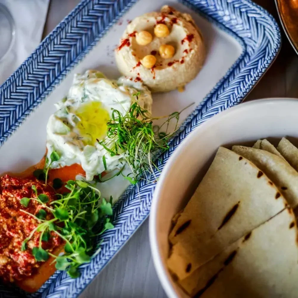 Rectangular platter with hummus, white dip, red dip, and pita bread.
