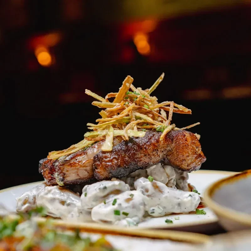Seared meat on mash, crispy fried topping, blurred bokeh background.