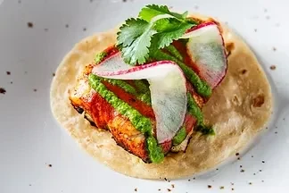 Single taco with spiced protein, green sauce, radishes, and cilantro.