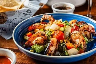 Golden-brown grilled shrimp and colorful vegetable salad in a blue bowl.