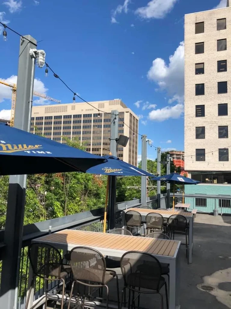 Empty elevated patio with high-top tables and blue Miller Time umbrellas.
