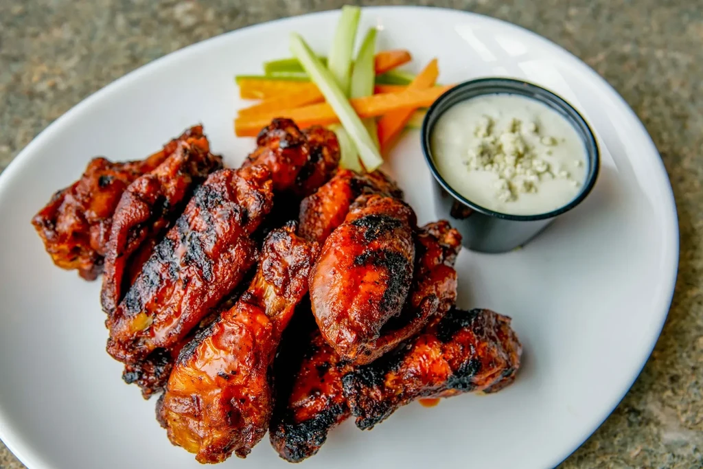 Plate of grilled chicken wings with blue cheese dip, celery, and carrots.