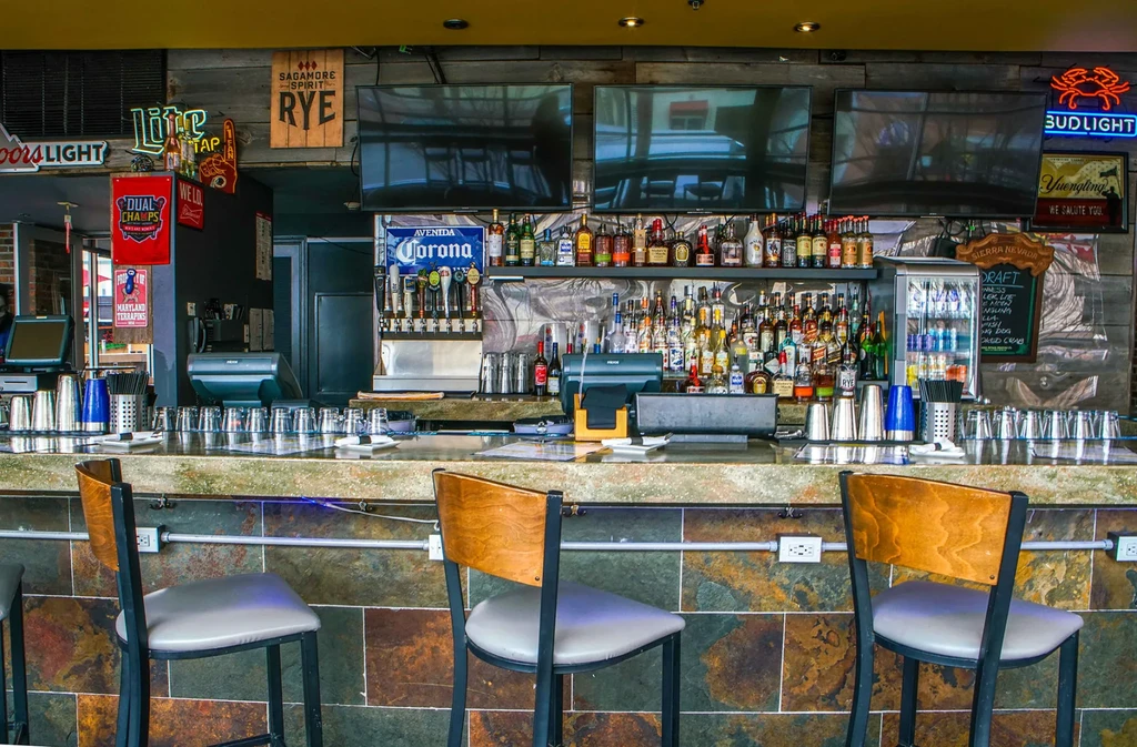 Vibrant, fully stocked bar interior with neon signs and bar stools.