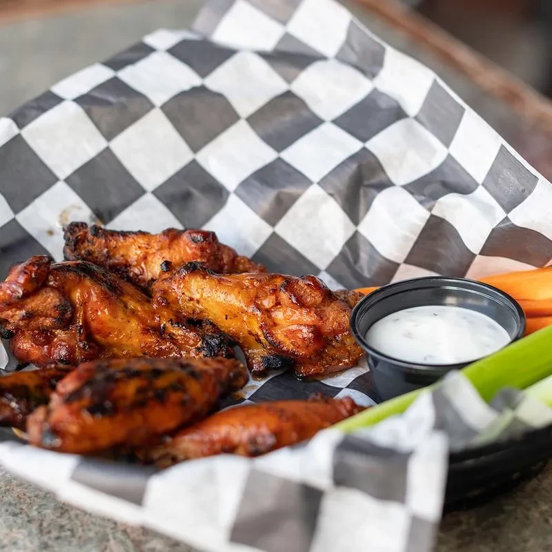 Grilled chicken wings with a glossy glaze, dip, and vegetables.