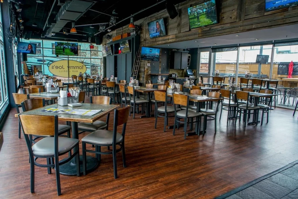 Empty industrial-chic restaurant with wooden tables, chairs, and multiple TVs.