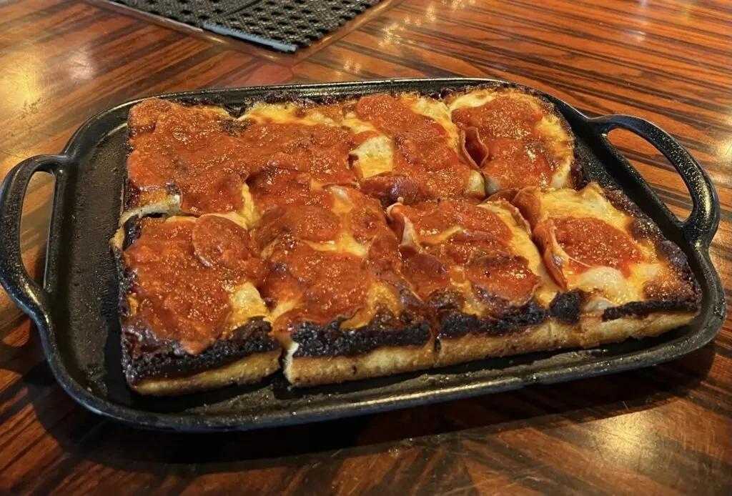 Rectangular deep-dish pepperoni and cheese pizza in cast iron pan.
