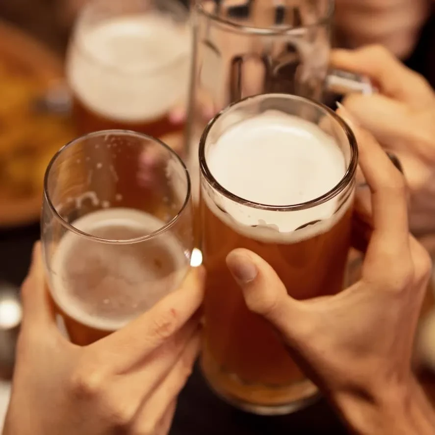 Multiple hands holding beer glasses in a toast.