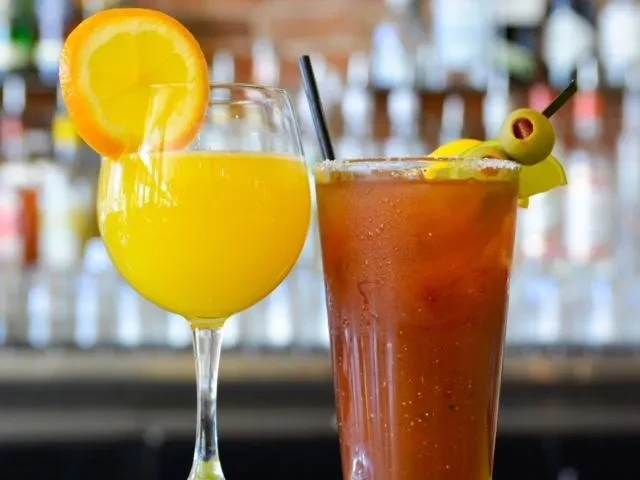 Brightly colored mimosa and Bloody Mary cocktails with garnishes at a bar.