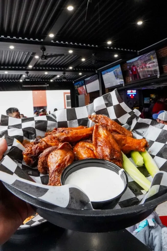 Crispy chicken wings with sauce and celery in a bustling sports bar.