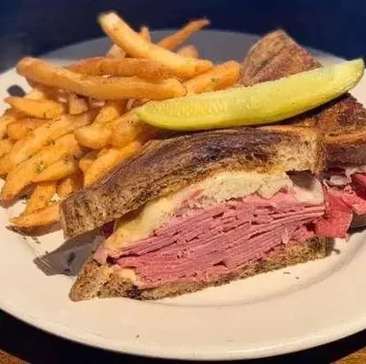Reuben sandwich cut in half, french fries, and dill pickle spear.