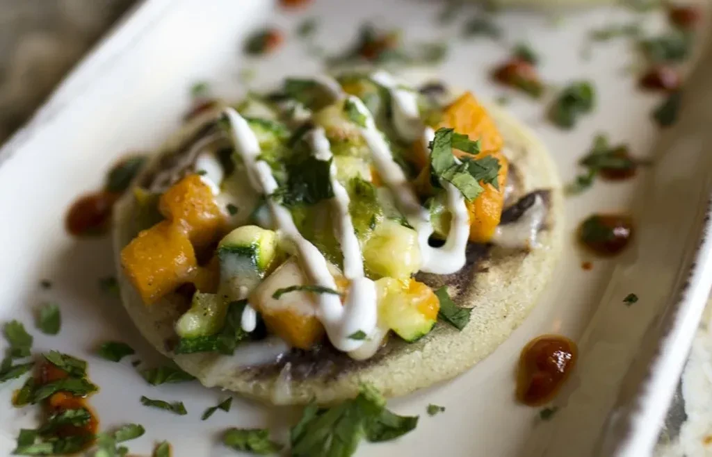 Flatbread topped with diced vegetables, creamy sauce, and green herbs.