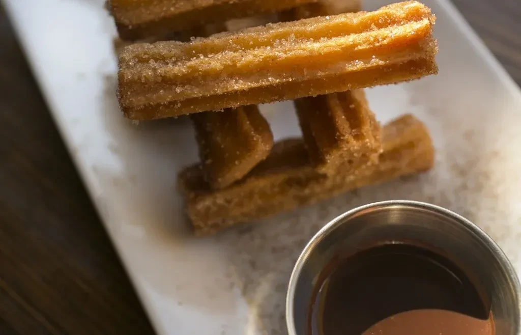 Golden-brown churros with sugar and cinnamon, served with chocolate sauce.