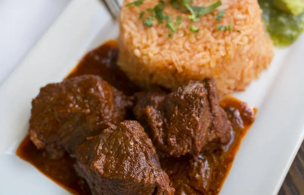 Overhead view: stewed meat, Spanish rice with herbs, and green salsa.