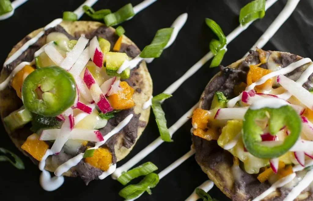 Two colorful mini tostadas topped with diced vegetables, jalapeño, and sauce.