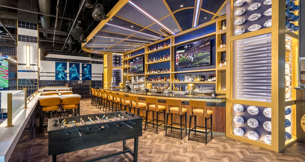 Modern sports bar interior with long bar, TVs, foosball, and athlete decor.