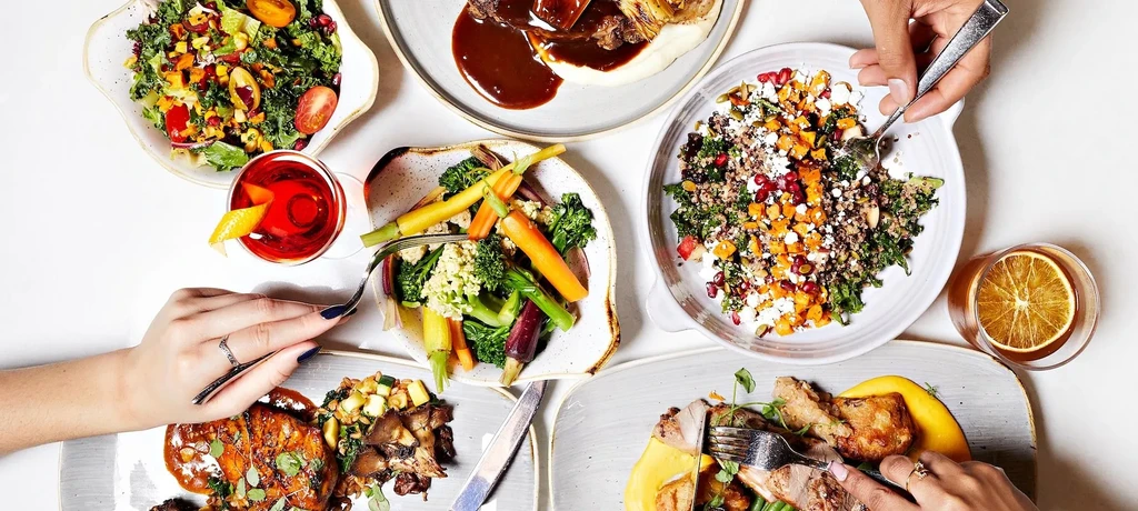 Overhead view of diverse, beautifully plated food, drinks, and hands dining.