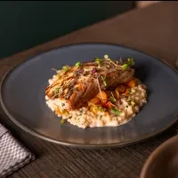 Plated grilled fish on creamy couscous with microgreens in restaurant.