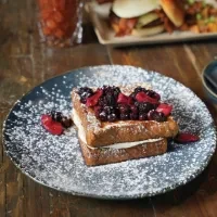 Stacked French toast with cream, berries, and powdered sugar on a dark plate.