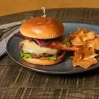 Close-up of a gourmet burger and crispy chips on a wooden table.