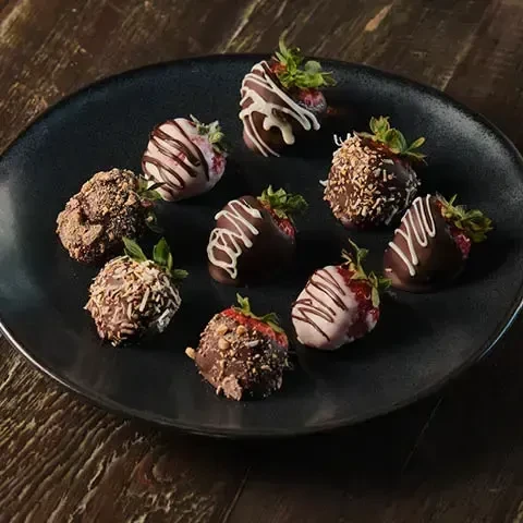Assorted chocolate-covered strawberries with toppings on a dark plate.