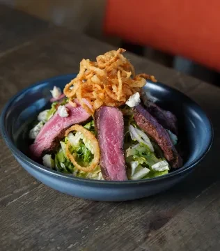 Steak salad with lettuce, crumbled cheese, and crispy fried onions.